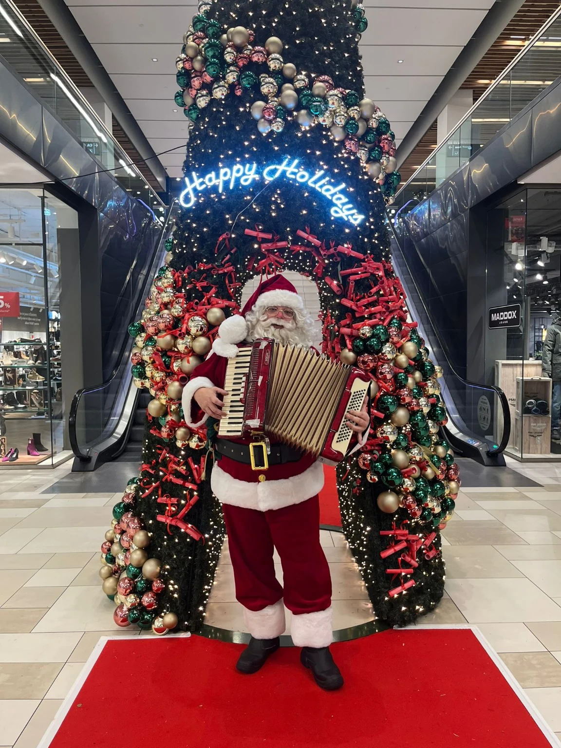 Kerstman met accordeon bij een grote kerstdecoratie in een winkelcentrum