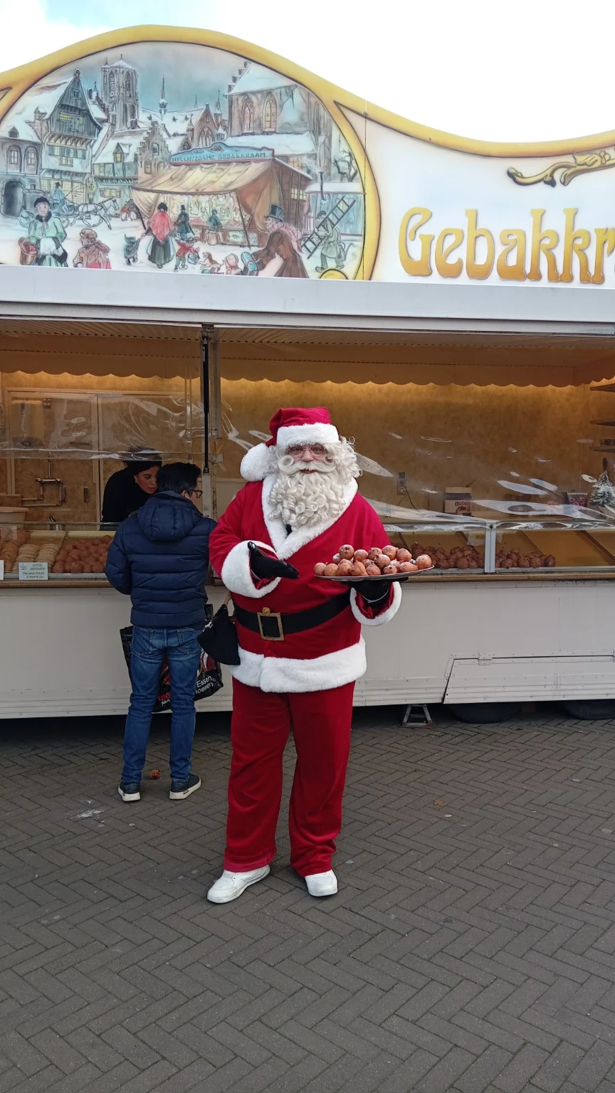 Kerstman bij een gebakkraam met oliebollen